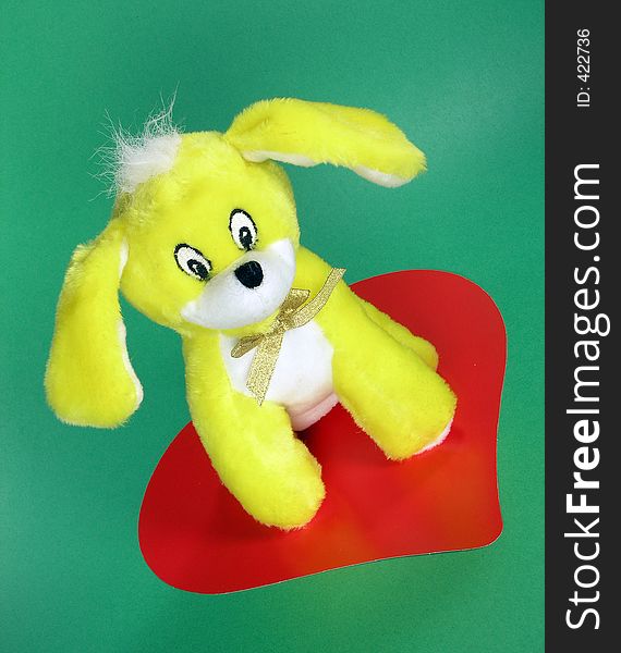 Stuffed yellow puppy dog on a red heart valentine symbol. Stuffed yellow puppy dog on a red heart valentine symbol
