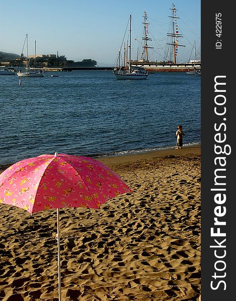 Pink umbrella in sand on beach in San Francisco, CA.