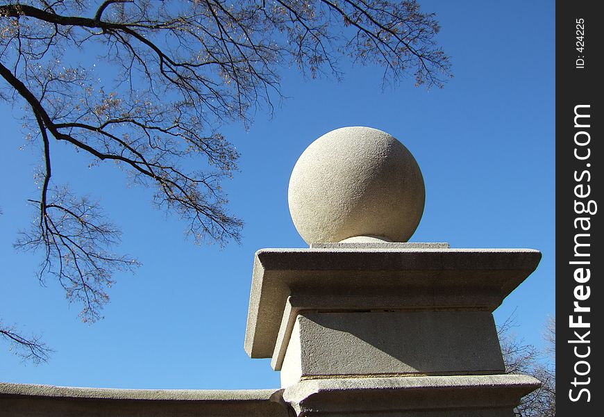 Stone sphere against blue sky and tree