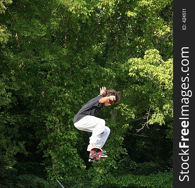 Male teen skateboarder jumping high with trees in background. Shot with a Canon 20D. Male teen skateboarder jumping high with trees in background. Shot with a Canon 20D