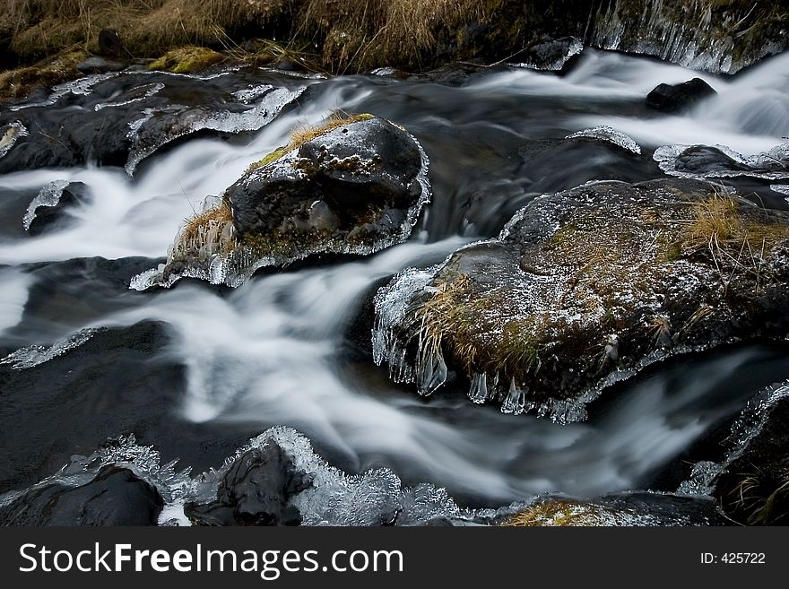 Water running around frozen stones in a stream. Water running around frozen stones in a stream