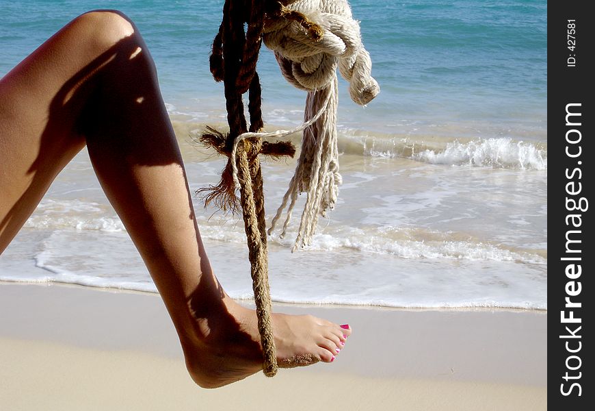Attractive woman's leg sways in a rope swing in the most beautiful beach in the world. Attractive woman's leg sways in a rope swing in the most beautiful beach in the world.