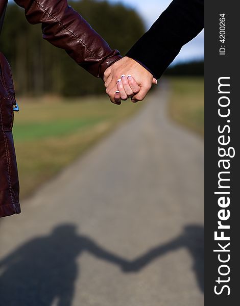 Two hands holding each other outdoor. Focus on hands, blurred way with shadow of the couple. Two hands holding each other outdoor. Focus on hands, blurred way with shadow of the couple.