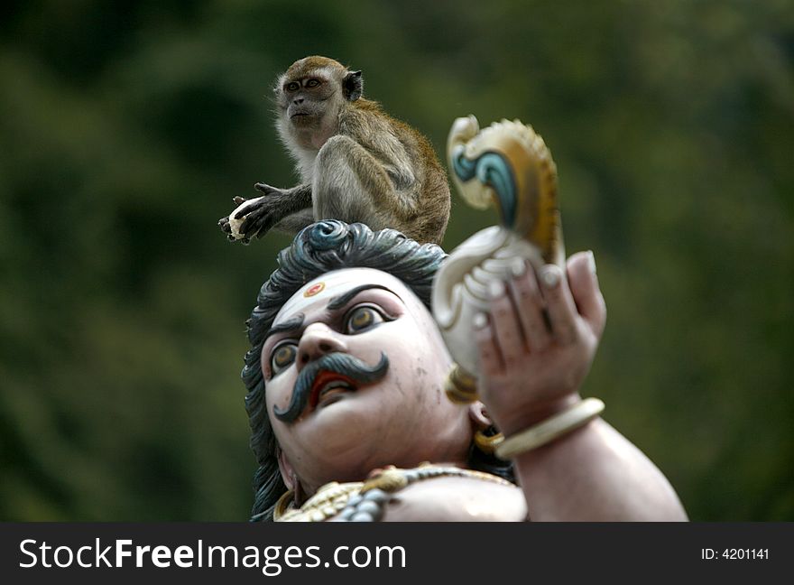 A monkey sits atop of a Hindu god statue with a green background.