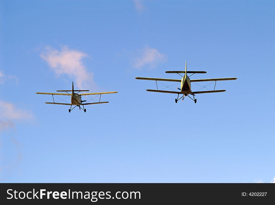 Two biplanes are flying from you on blue sky