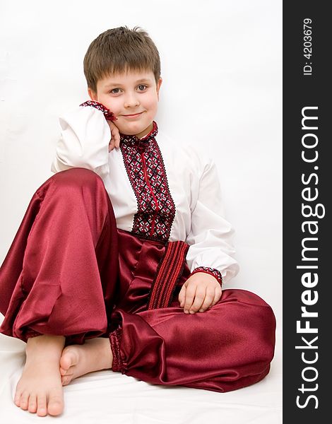 A boy in red trousers and white shirt sits thoughtful