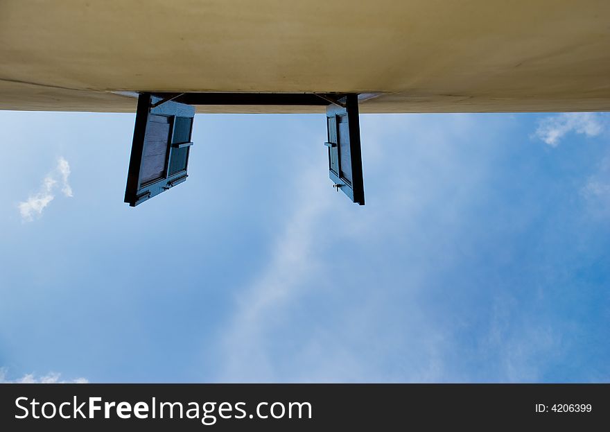 Opened windows on upper storey seen against a partly cloudy blue sky