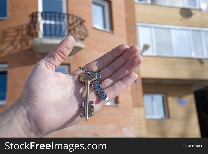 On a background of a modern brick house, hand with keys from an apartment. On a background of a modern brick house, hand with keys from an apartment.