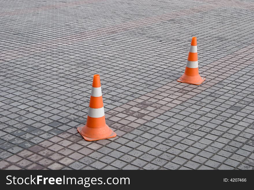 Two red highway cones on paving block