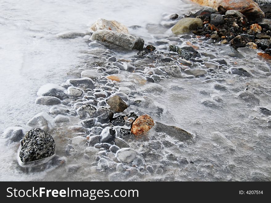 A frozen river stream with colorful stones under it. A frozen river stream with colorful stones under it