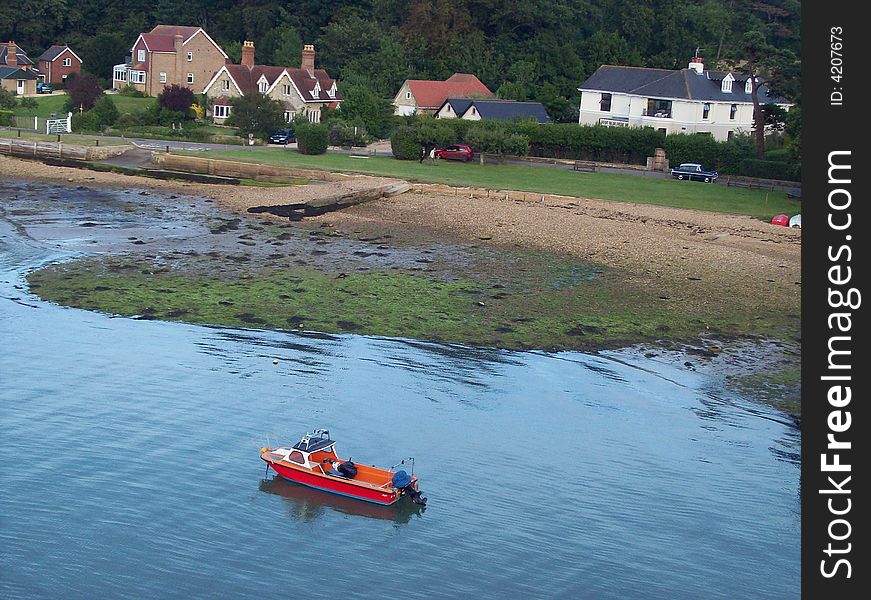 Photo of a small red boat near an English coast with houses. Photo of a small red boat near an English coast with houses