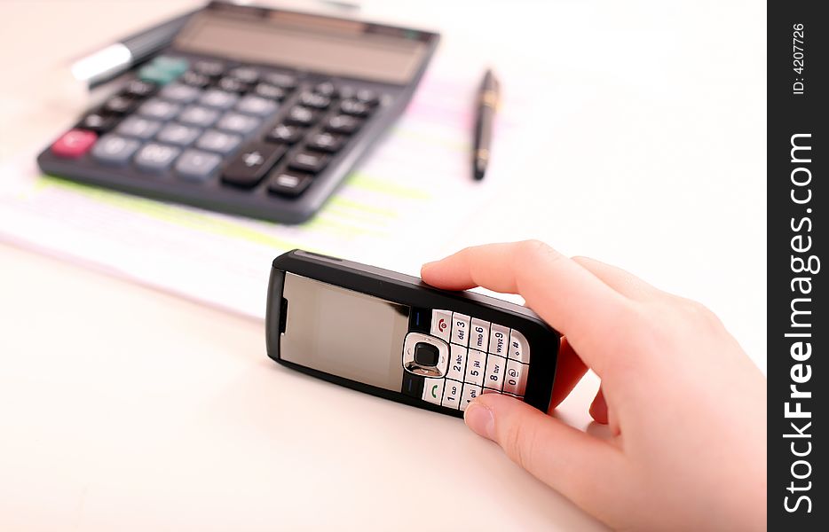 Cell phone in the female hand under the desk. Cell phone in the female hand under the desk