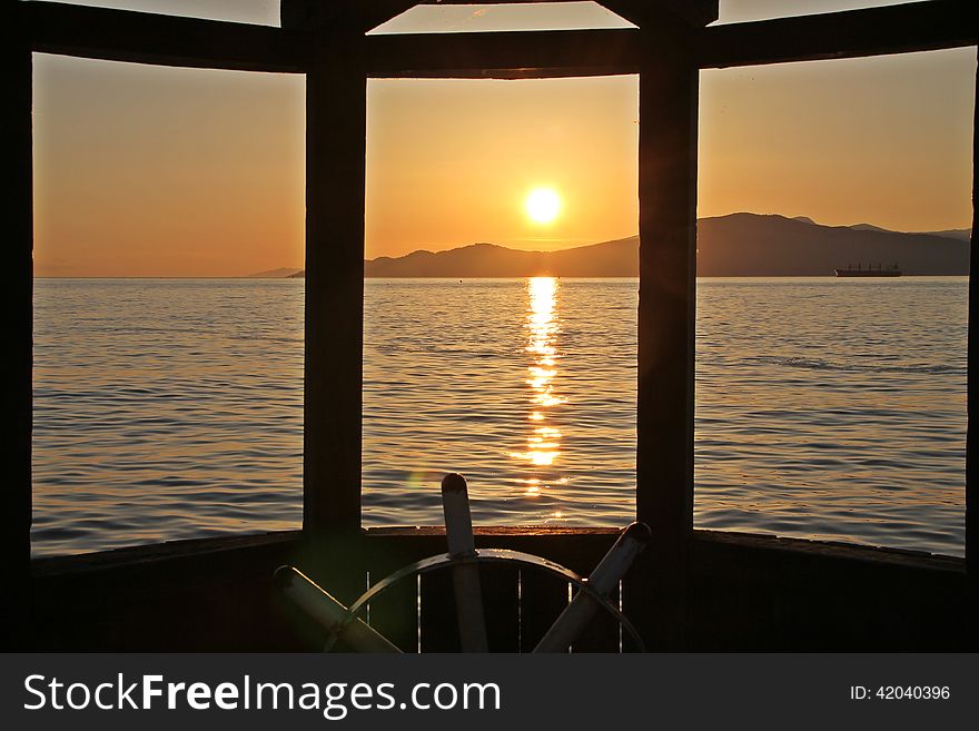 Sunset at Vancouver Bay, Canada, steering wheel and wooden window frame in foreground. Sunset at Vancouver Bay, Canada, steering wheel and wooden window frame in foreground
