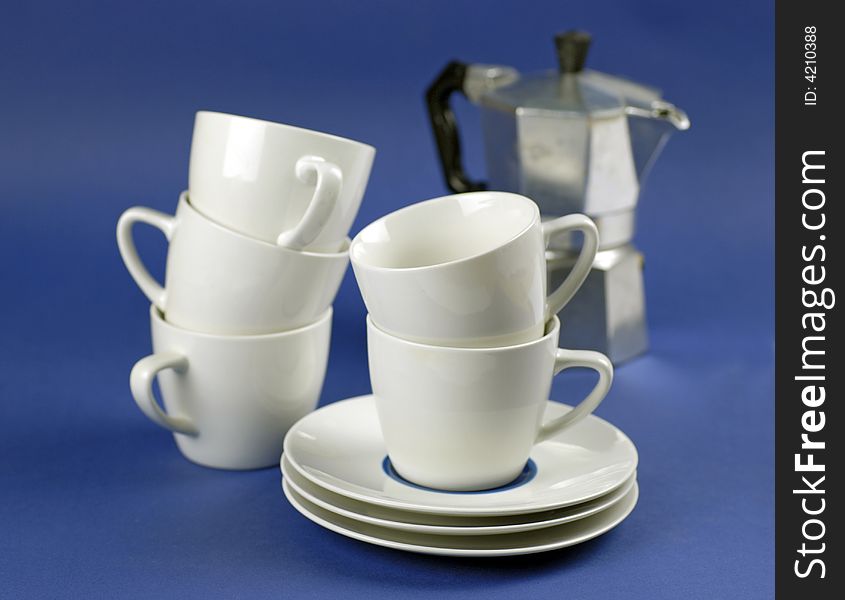 Espresso coffee cups, saucers and espresso machine on blue ground; differential focus