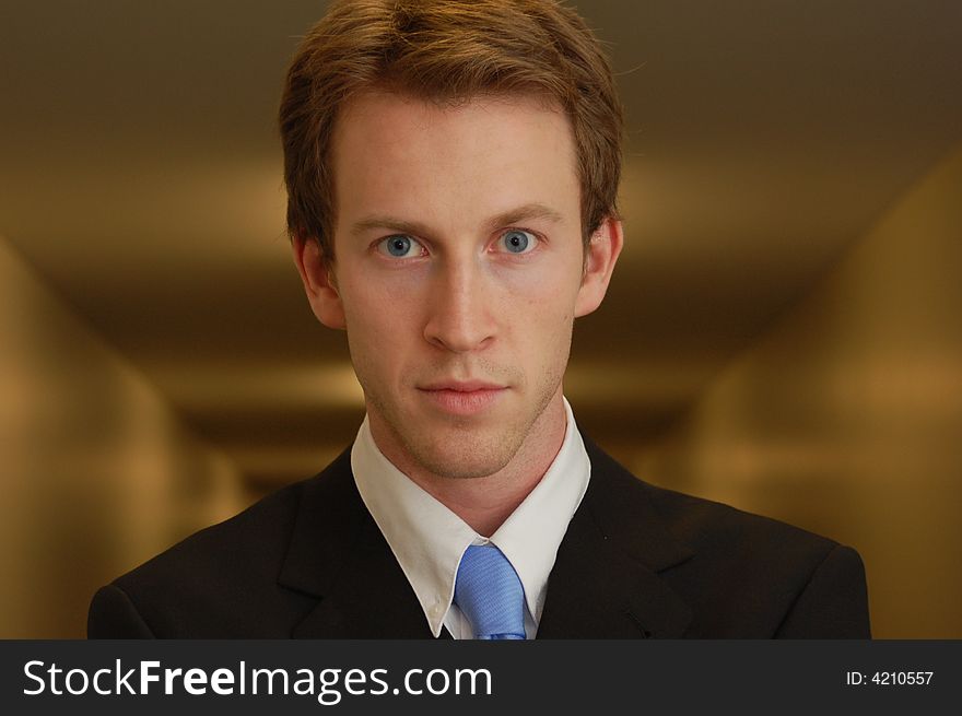 A young man in a black suit stands in an empty hallway with his arms crossed looking into the camera. A young man in a black suit stands in an empty hallway with his arms crossed looking into the camera