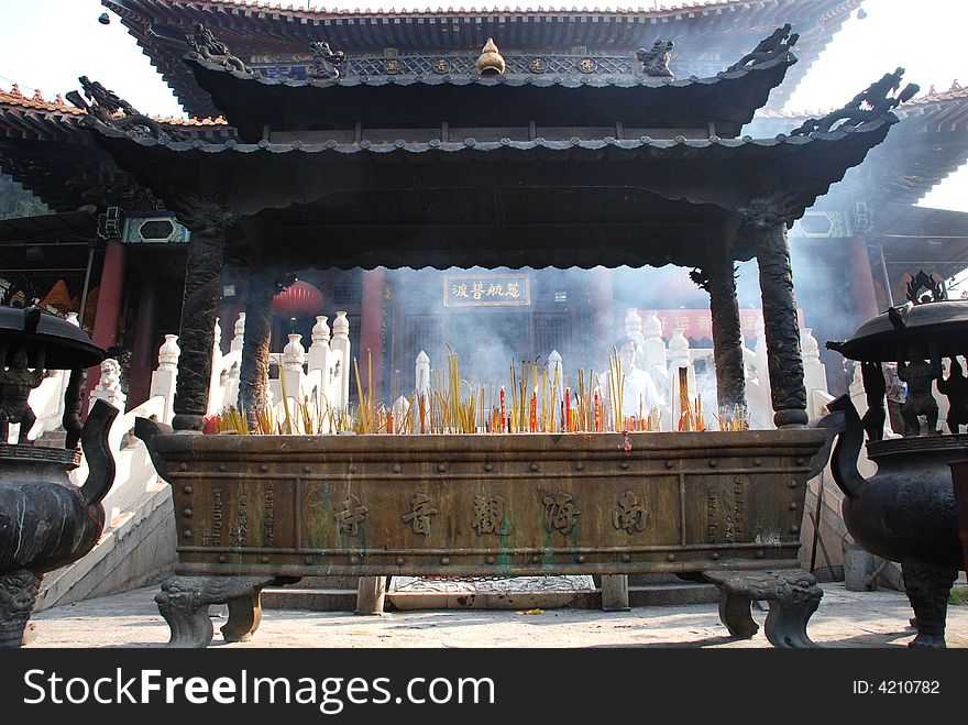 Joss sticks and candles burning at a temple， in a bronze incense burner in a buddhist temple。. Joss sticks and candles burning at a temple， in a bronze incense burner in a buddhist temple。