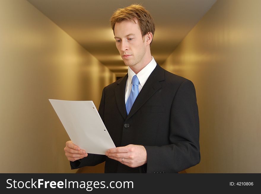 A young man in a black suit stands in an empty looking at a piece of paper. A young man in a black suit stands in an empty looking at a piece of paper