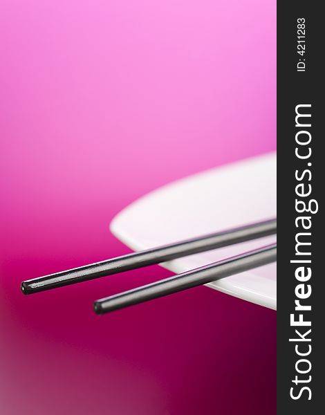 Chopsticks on the white plate over pink background