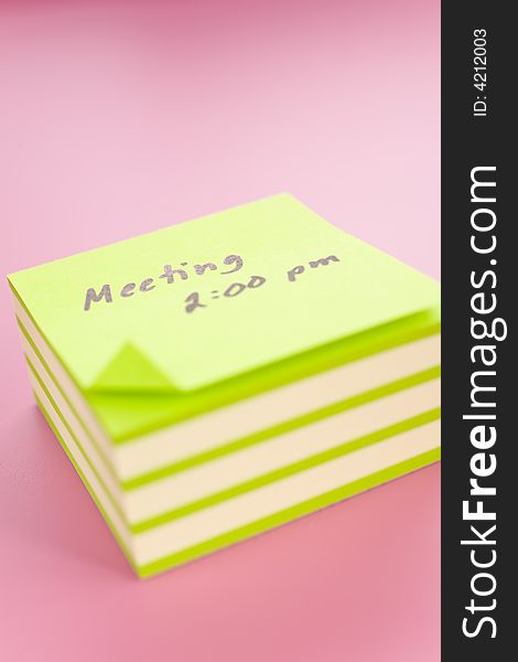 Pile of sticky notes with meeting reminder text over a pink table