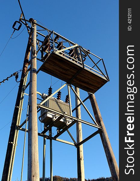 The electric transformer on a iron mast on the background of blue sky.Distant village in mountains ,Thirol, Austria