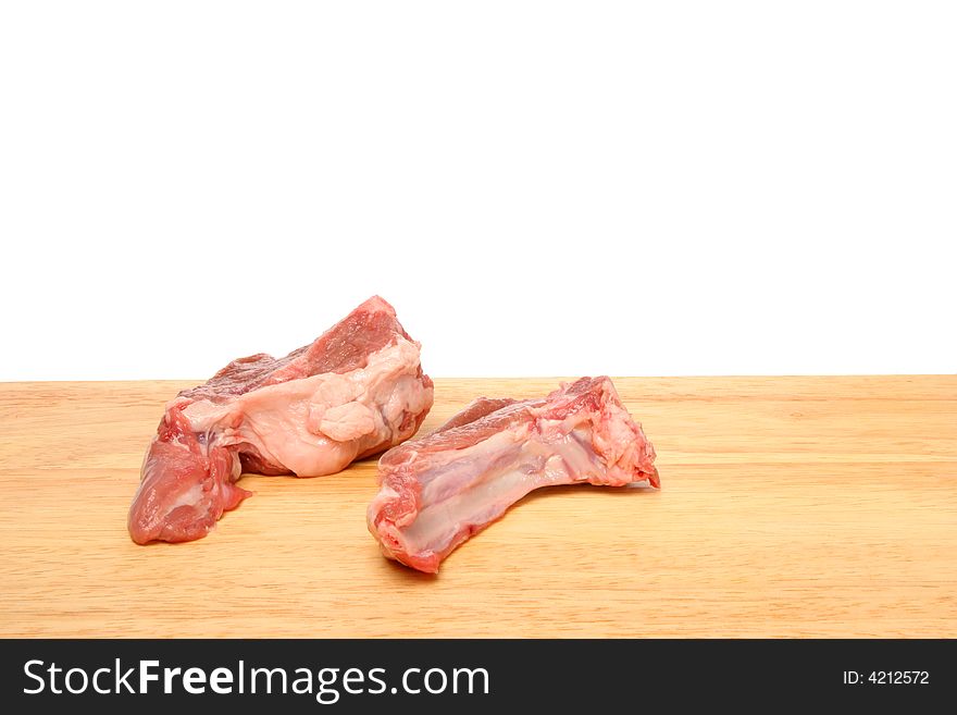 Two raw lamb chops on wooden food preparation board against white