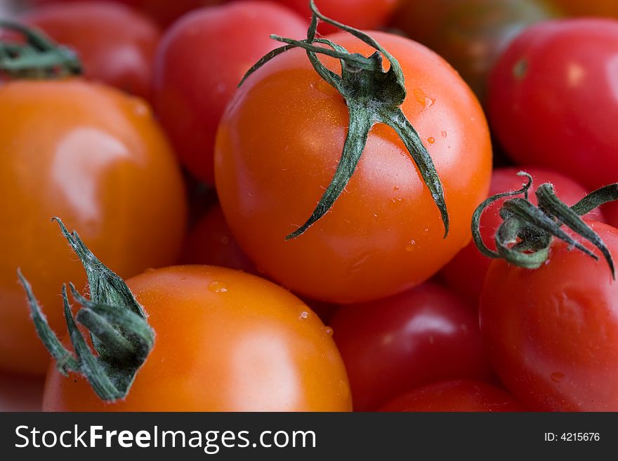 Grouping of fresh, firm orange and red cherry tomatoes, with water