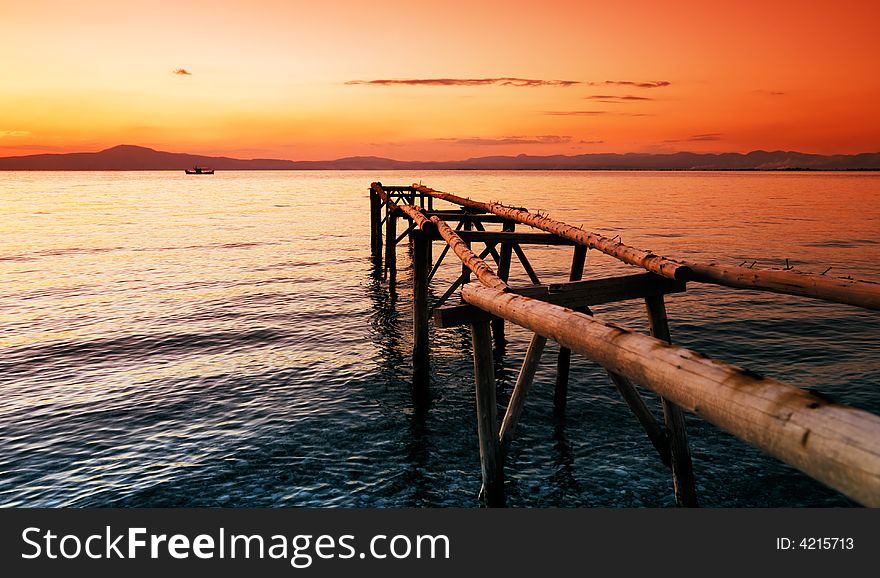 A primitive wooden pier, photographed during a glorious sunset, extends into the sea and leads the eye to a fishing boat in the distance. A primitive wooden pier, photographed during a glorious sunset, extends into the sea and leads the eye to a fishing boat in the distance.