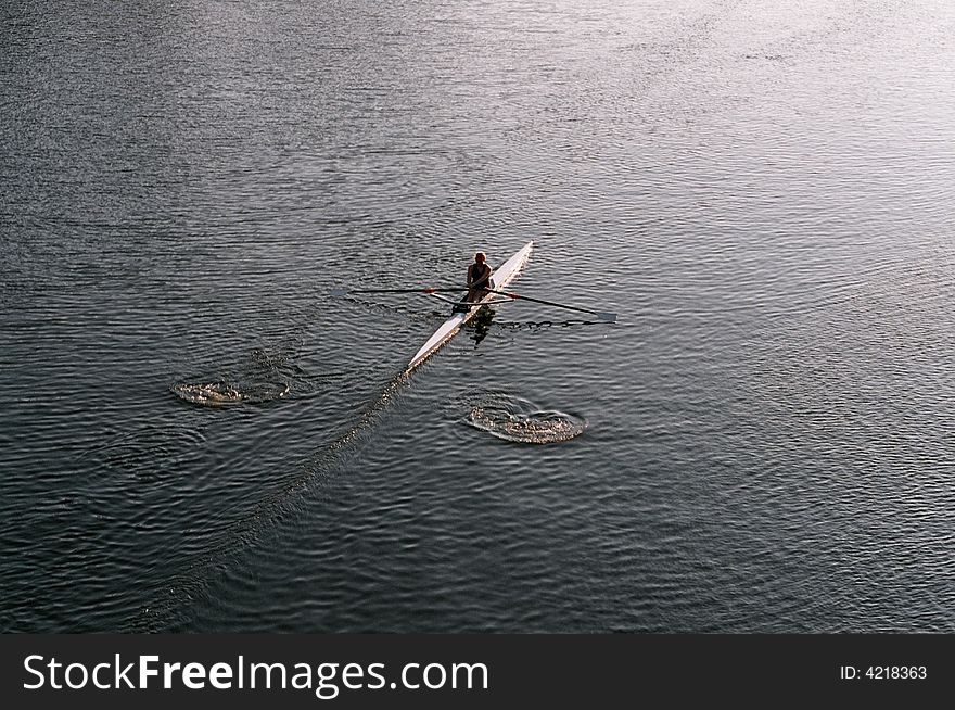 A lone rower on a river early in the morning