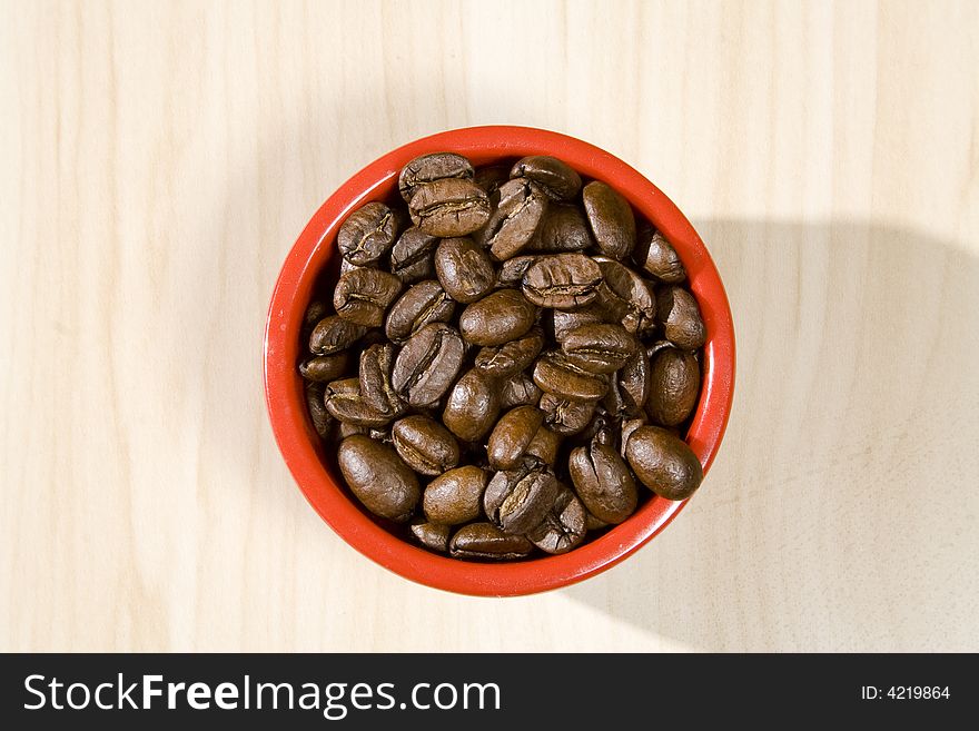 Close up of a red bowels full of coffee beans on a wood grain table. Selective focus. Close up of a red bowels full of coffee beans on a wood grain table. Selective focus.