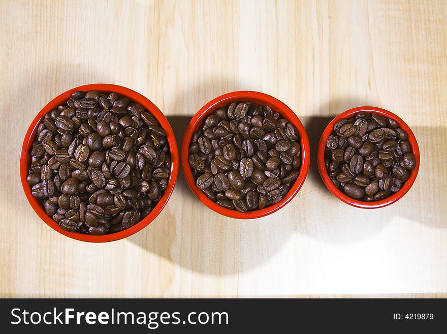 3 red bowels full of coffee beans on a wood grain table. 3 red bowels full of coffee beans on a wood grain table