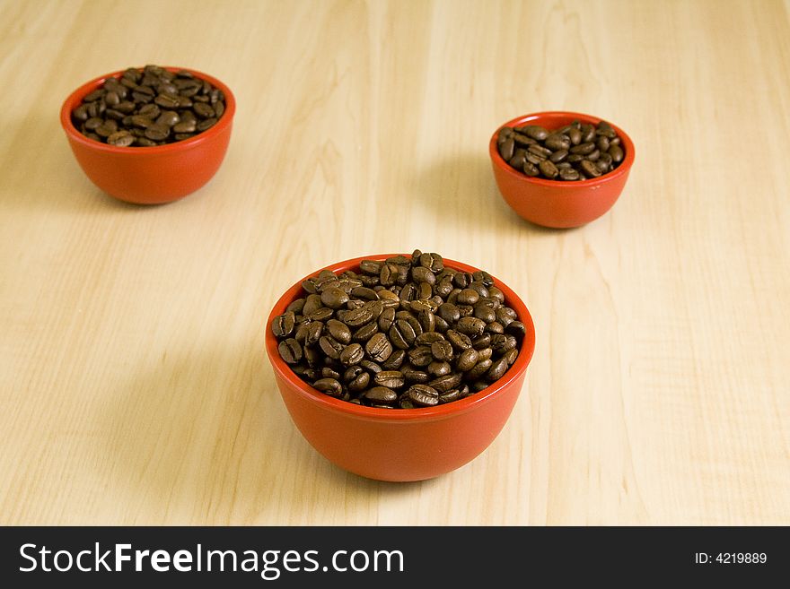 3 red bowels full of coffee beans on a wood grain table. 3 red bowels full of coffee beans on a wood grain table