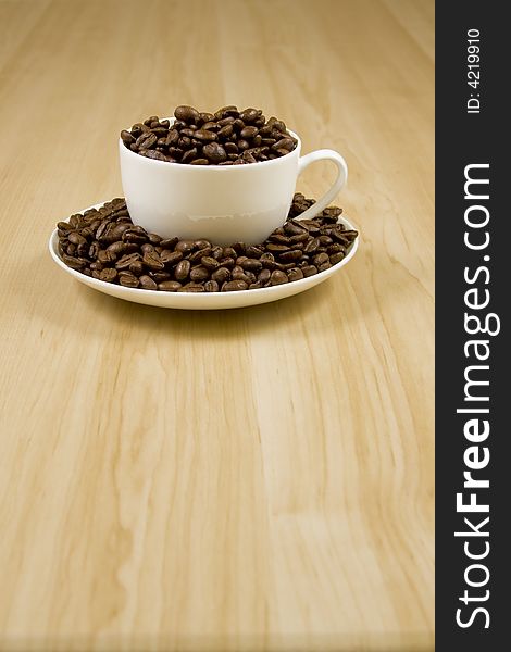 White coffee cup full of coffee beans on a wood rain table. White coffee cup full of coffee beans on a wood rain table.