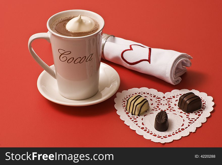 A mug of hot cocoa with 3 chocolates and a napkin with a Valentine's Day heart on it. A mug of hot cocoa with 3 chocolates and a napkin with a Valentine's Day heart on it.