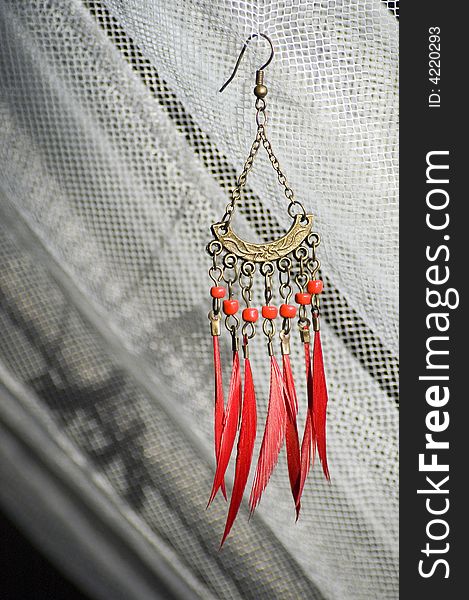 Red earring with feather hanging on a web
