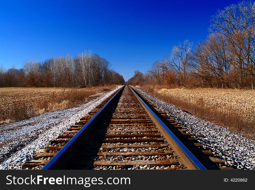 Railroad tracks disappear to the horizon under a bright blue ski. Railroad tracks disappear to the horizon under a bright blue ski.