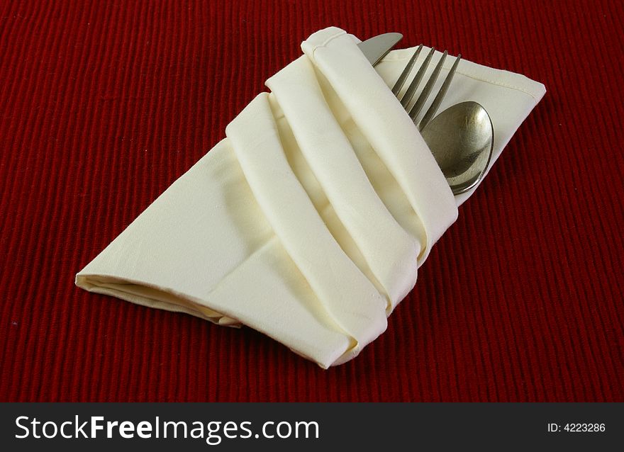 Fancy folded linen cream colored napkin with fork, knife, spoon, on deep red textured background. Fancy folded linen cream colored napkin with fork, knife, spoon, on deep red textured background.
