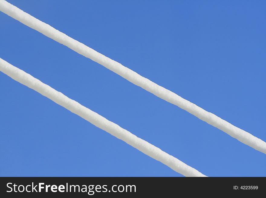 Two snow-covered wires on a background of the blue sky