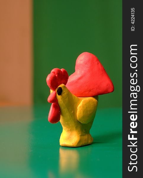 Toy plasticine cock with red heart on top of it