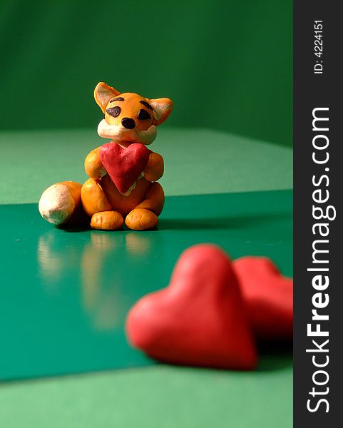 Toy cute plasticine fox with heart in its hands and 2 hearts in front of photo