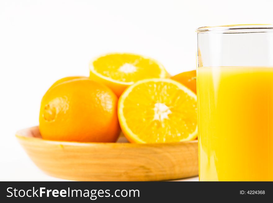 Two halves of orange in a wooden bowl with uncut oranges and a glass of orange juice in the foreground