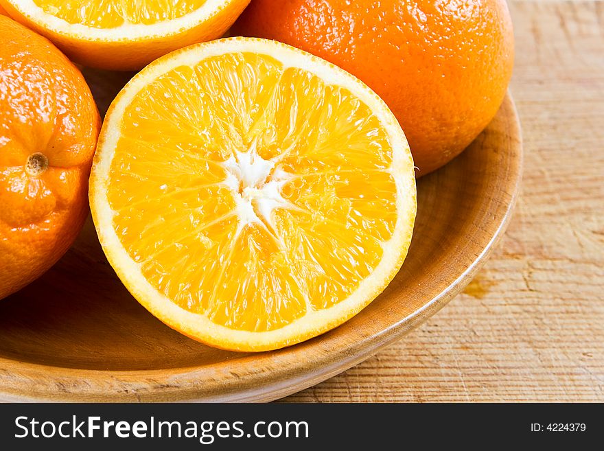 Two halves of orange in a wooden bowl with uncut oranges