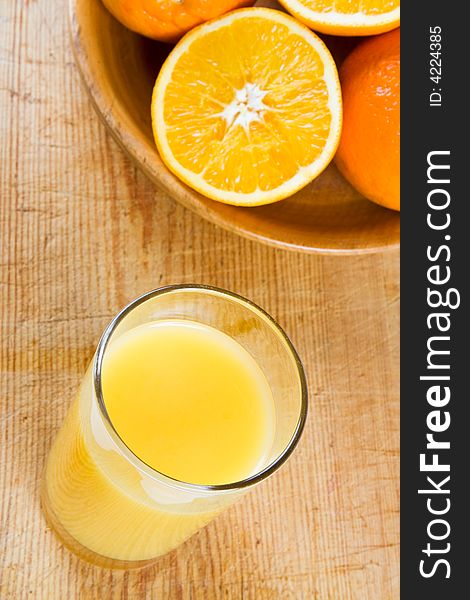 Half an orange in a wooden bowl with uncut oranges and a glass of orange juice in the foreground. Half an orange in a wooden bowl with uncut oranges and a glass of orange juice in the foreground