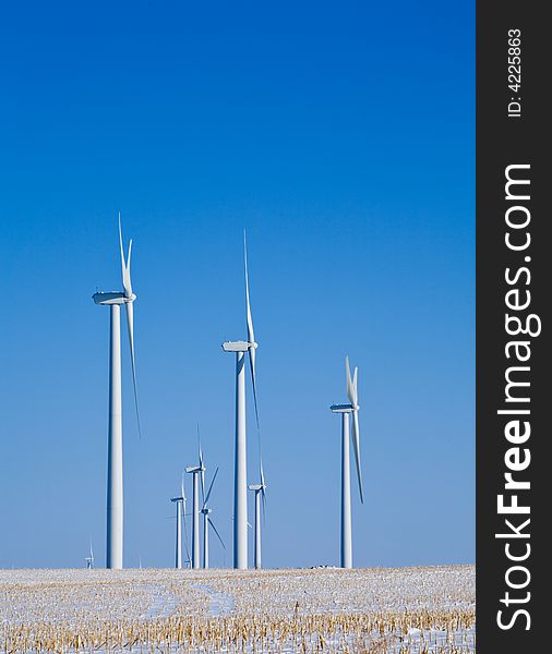 Group of wind turbines in corn field with blue sky and snow. Group of wind turbines in corn field with blue sky and snow