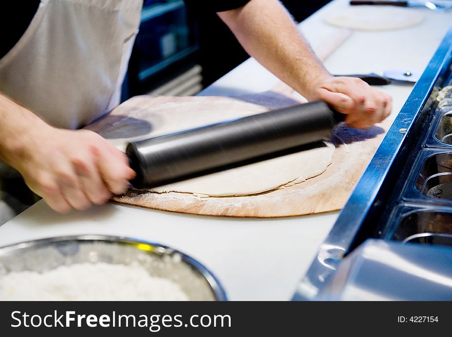 Rolling out dough for pizza with pin in motion. Rolling out dough for pizza with pin in motion