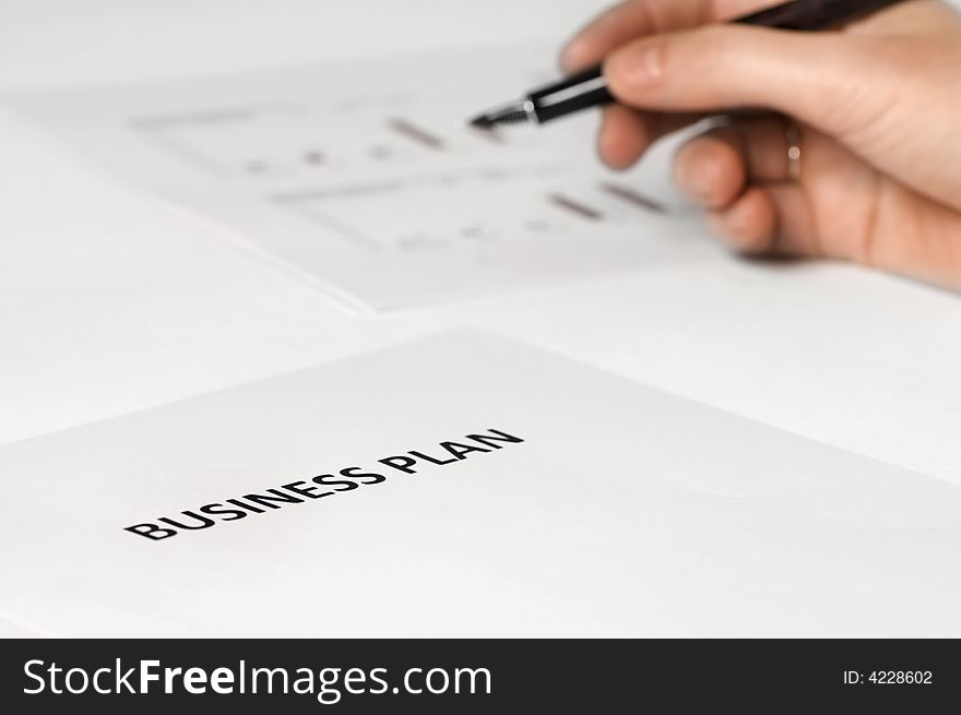 Paper on desk with business plan on it. hand holding pen. paper with graphics on the background. Paper on desk with business plan on it. hand holding pen. paper with graphics on the background.