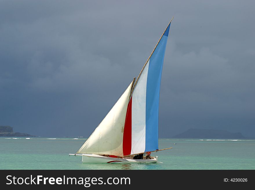 Multi-coloured sailed pirogue in front of dark clouds in a regatta in the north of Mauritius