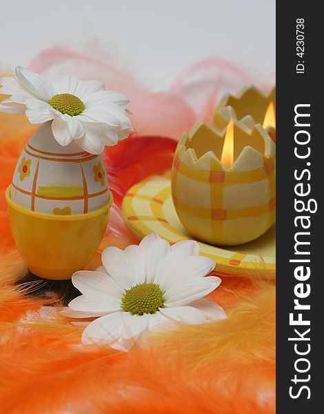 Easter egg and candle with white flowers and pink and orange feathers.