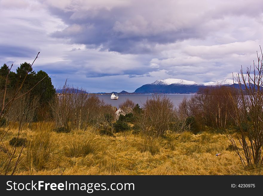 In the nice and wild norway country, a landscape from winter time with land, ocean and mountains in the offing. In the nice and wild norway country, a landscape from winter time with land, ocean and mountains in the offing