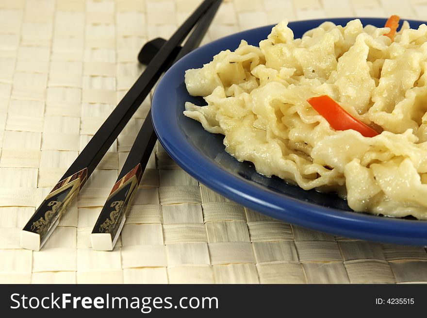 Blue plate with chinese noodles with vegetables and chopsticks on mat