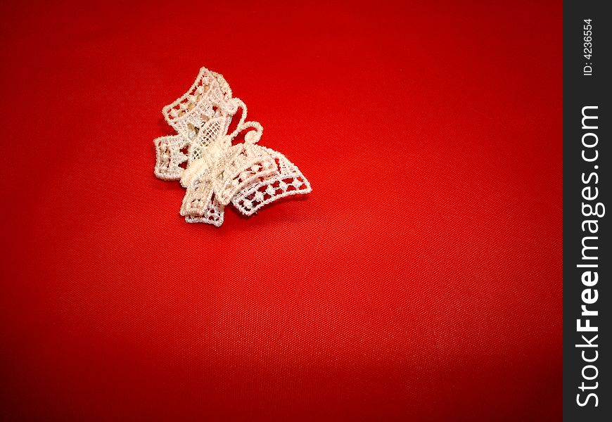 A small white crocheted butterfly on a red background. A small white crocheted butterfly on a red background.